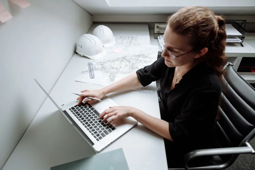 Aan het werk achter de laptop, tussen tekeningen en helmen